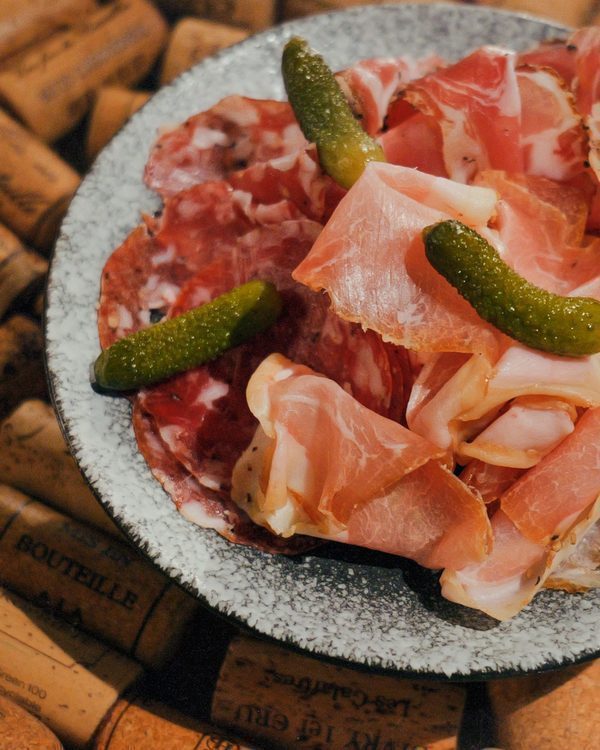 A charcuterie plate of cured meats and cornichons on a stone plate at CORKS