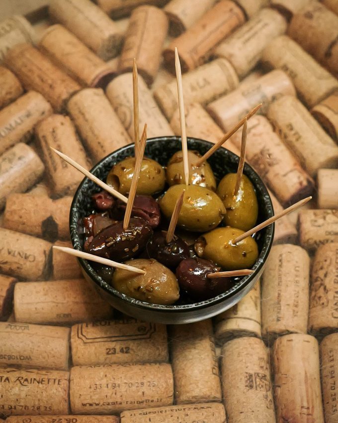 A bowl of marinated olives set on a bed of used wine corks at CORKS