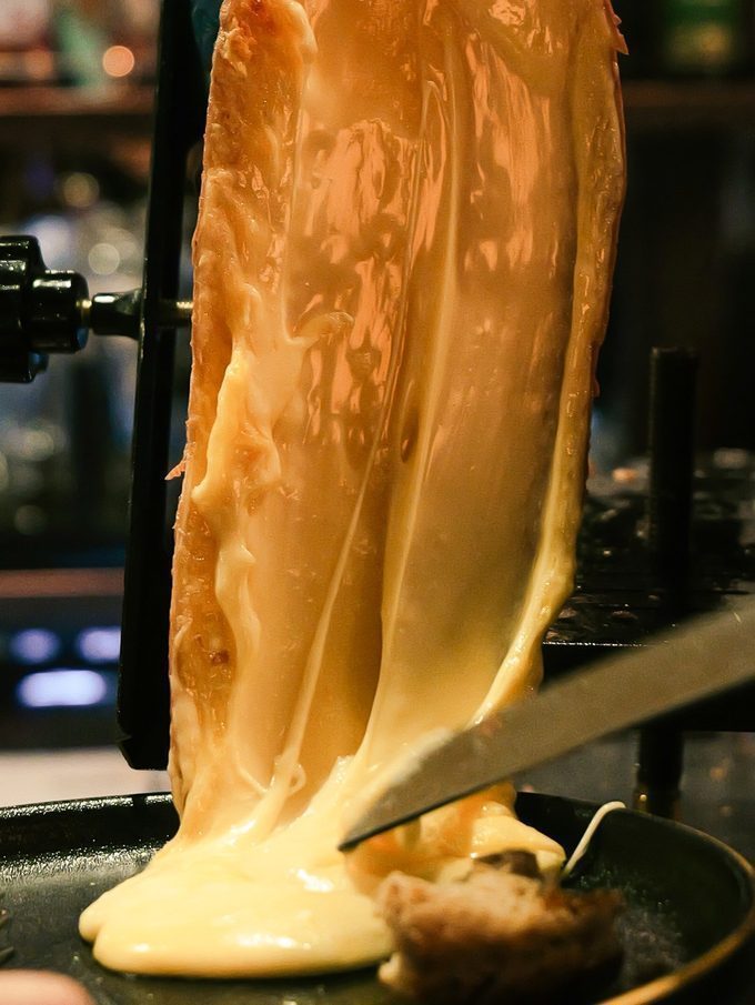 Melted raclette being scraped over the plate at CORKS