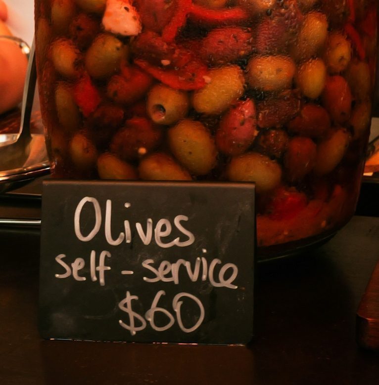 The jar of marinated olives on the CORKS counter beside its self service chalkboard