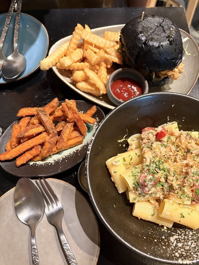 A table spread of black bun burger, crinkle fries, sweet potato fries and rigatoni