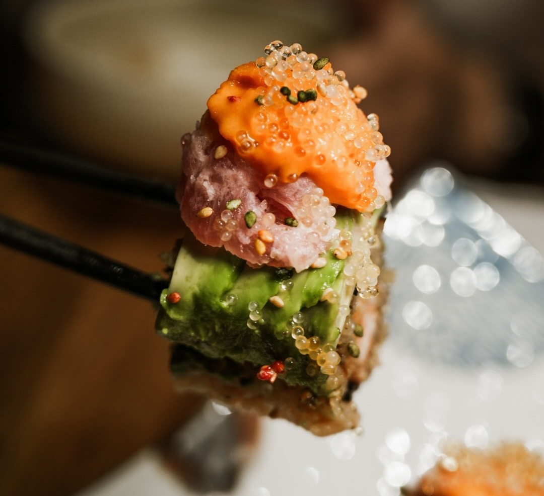 The Godzilla roll lifted on chopsticks, topped with uni and tobiko, at Kuki Izakaya