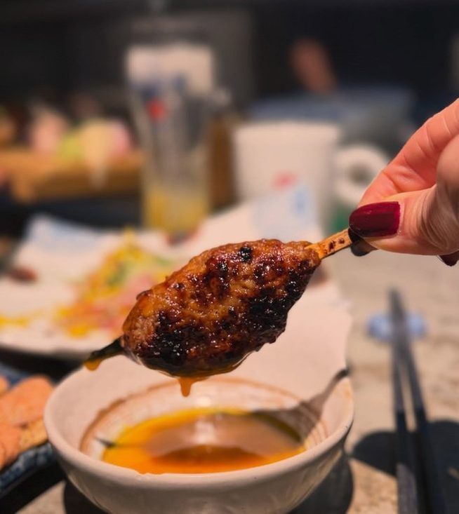 A yakitori skewer held over the dipping egg at Kuki Izakaya