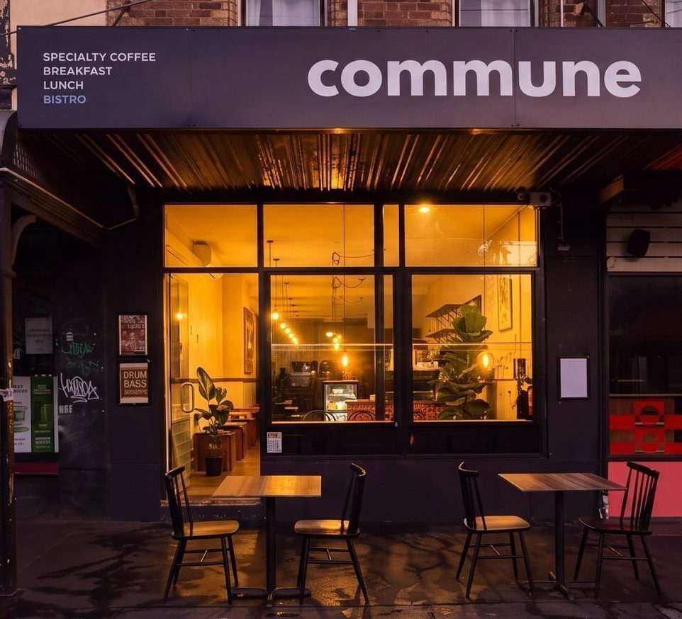 The Commune storefront at dusk, the black awning lit over Brunswick Street