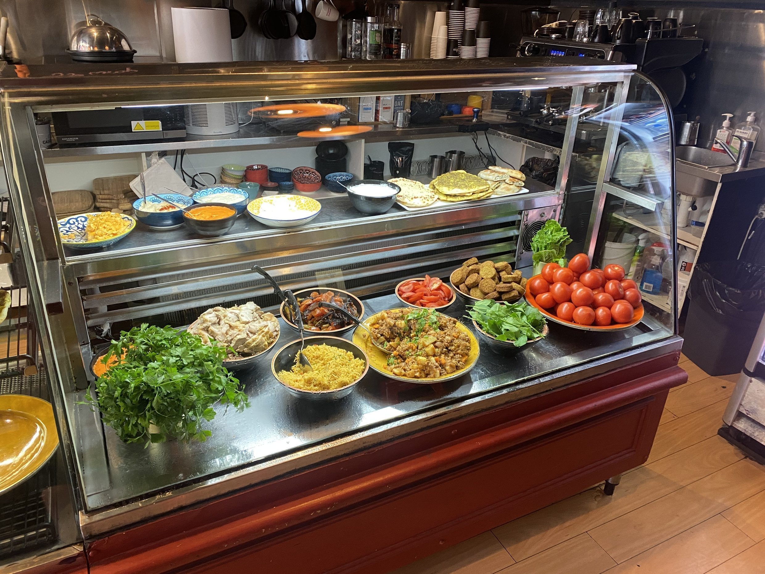 The display cabinet at Little Bridge Cafe, loaded with mezze: hummus and labneh in painted bowls, spiced rice, falafel, roast chicken, tomatoes and fresh parsley