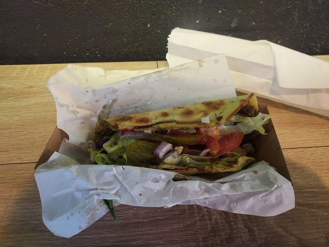 Za'atar wrap opened in its takeaway box with lettuce, tomato, pickles and red onion
