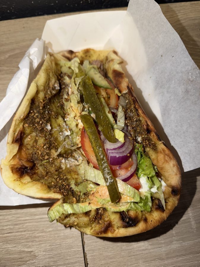 Open za'atar mana'ish loaded with salad, pickles, tomato and garlic sauce before rolling