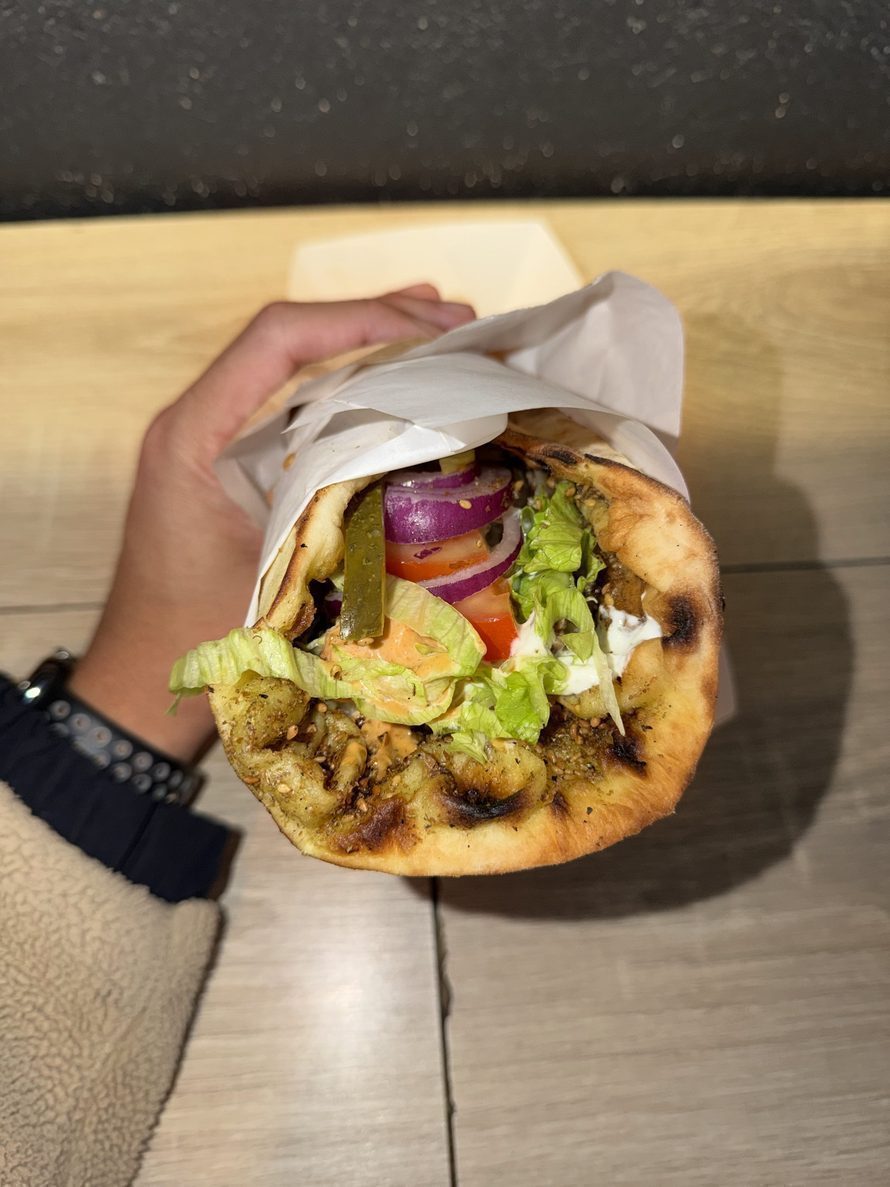 A hand holding a rolled Little Bridge wrap, salad, pickles and red onion tucked into grilled flatbread